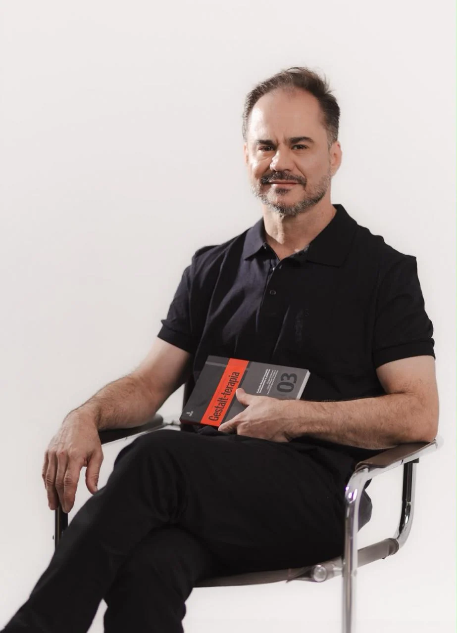 Marcelo Favoretto sentado em uma poltrona, segurando um livro de Gestalt-terapia